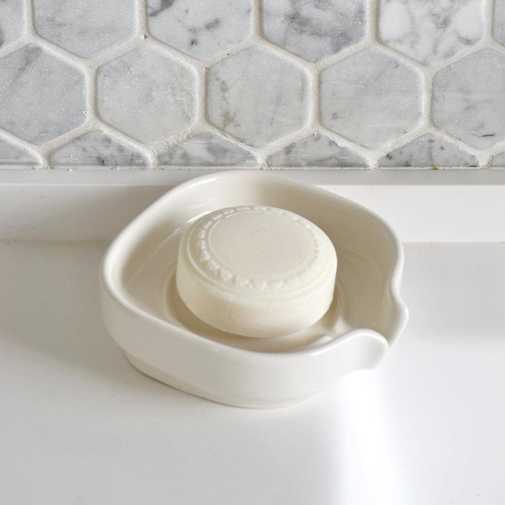 White glossy porcelain self-draining soap dish with soap bar resting inside
