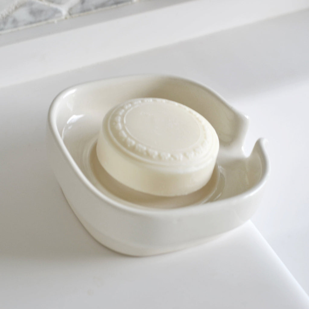 White glossy porcelain soap dish with side handle opening and soap bar