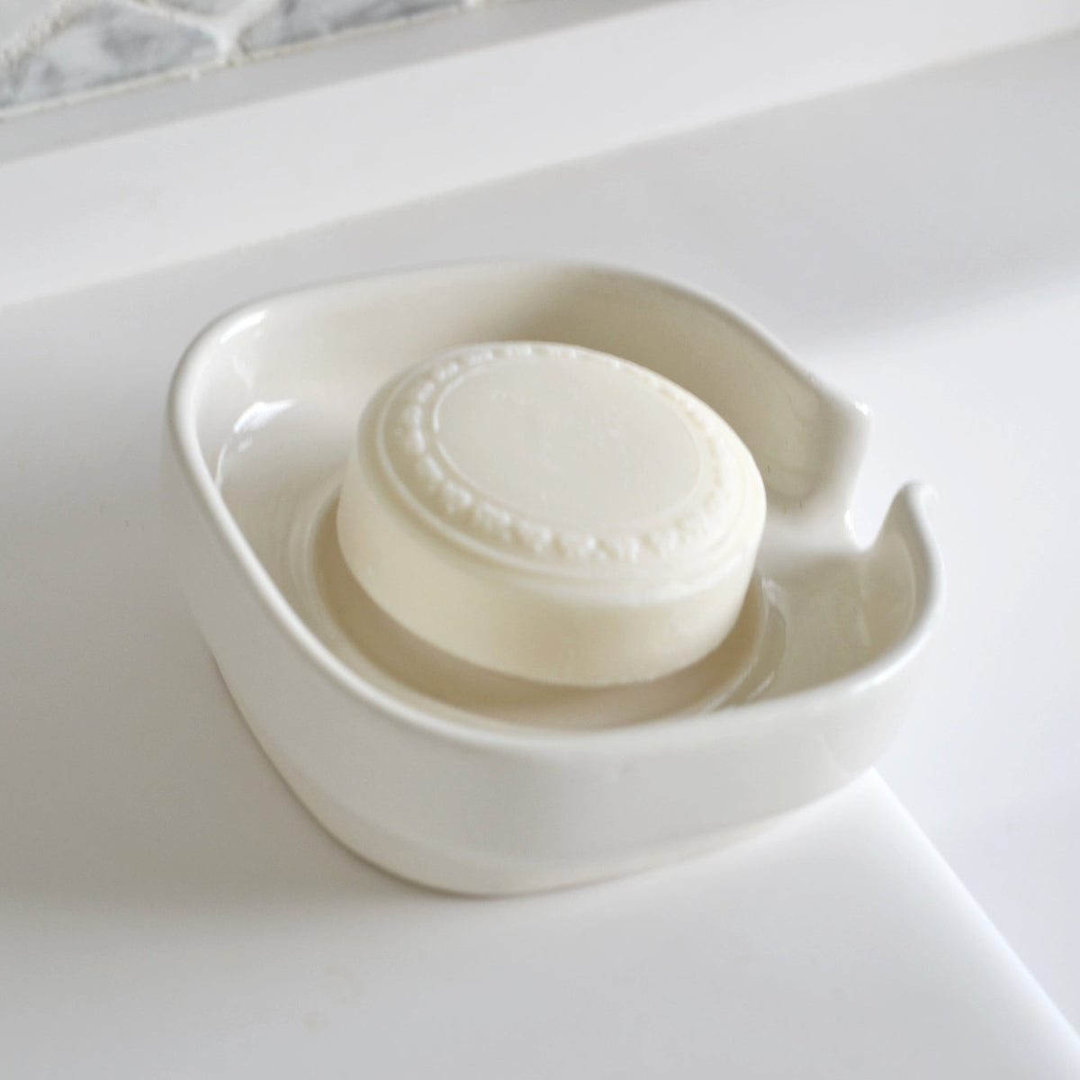 White glossy porcelain soap dish with side handle opening and soap bar