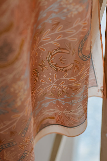Dusty rose wild rag scarf close-up with floral sprays and paisley accents along edge