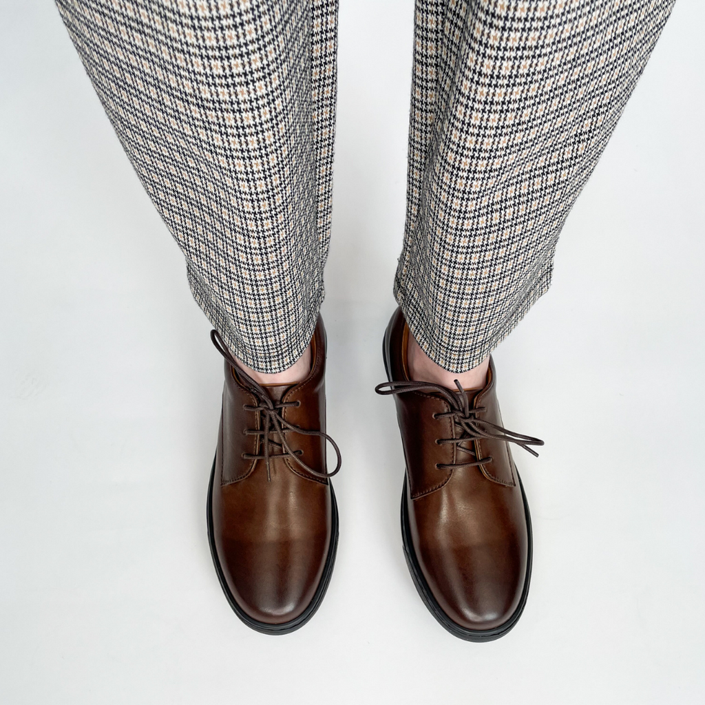 Brown lace-up dress shoes on feet with black rubber soles and eyelet lacing