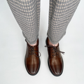 Brown lace-up dress shoes on feet with black rubber soles and eyelet lacing