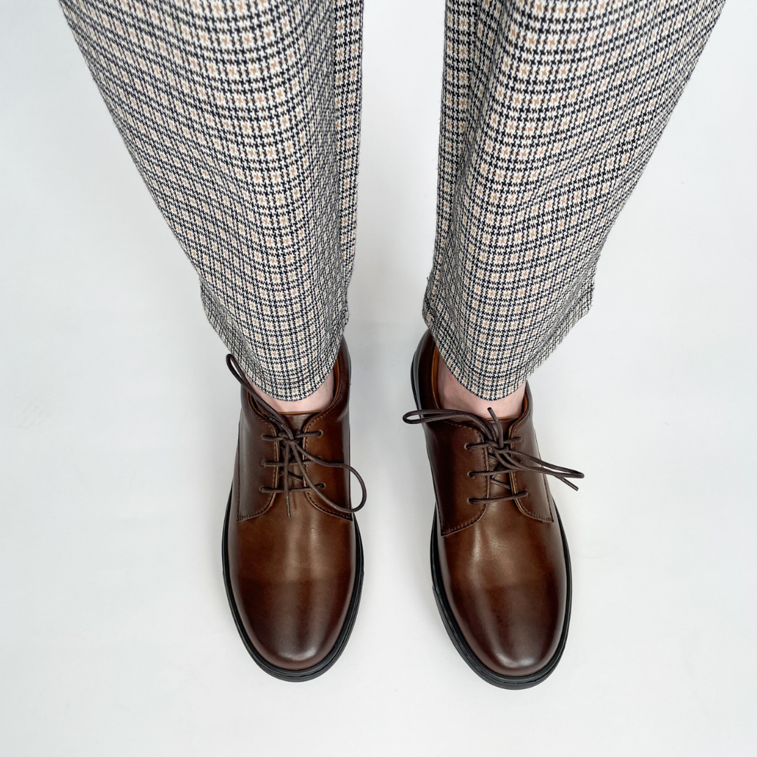 Brown lace-up dress shoes on feet with black rubber soles and eyelet lacing