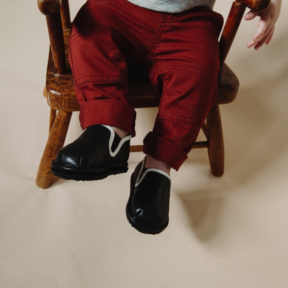 Kids' easy-on barefoot shoes, black slip-on with white trim on red pants