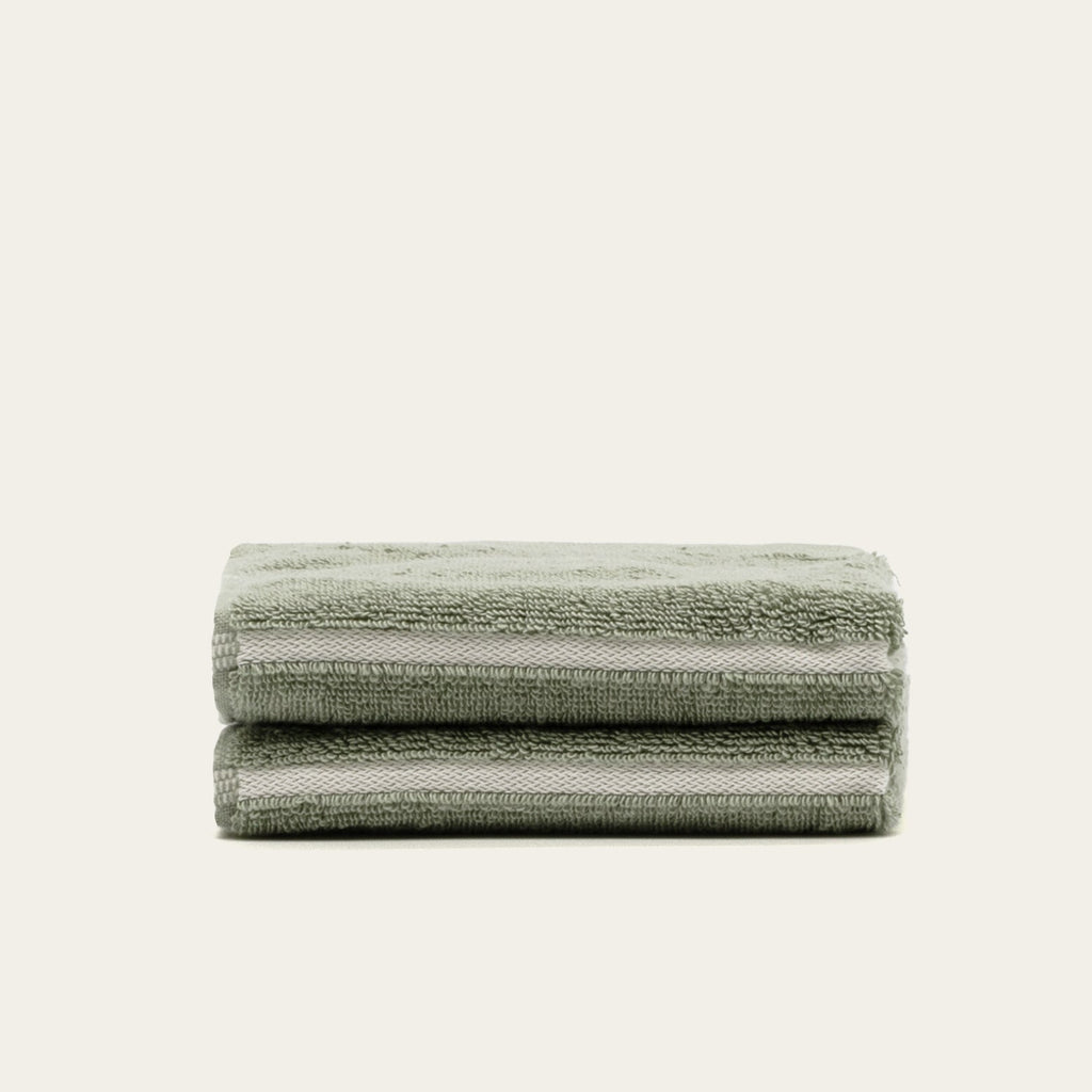 Stack of sage green cotton towels with ribbed texture, folded