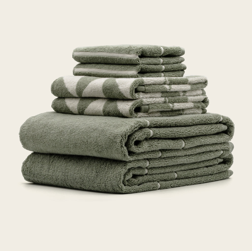 Sage cotton terry towels, stacked in folded layers with textured looped surface.
