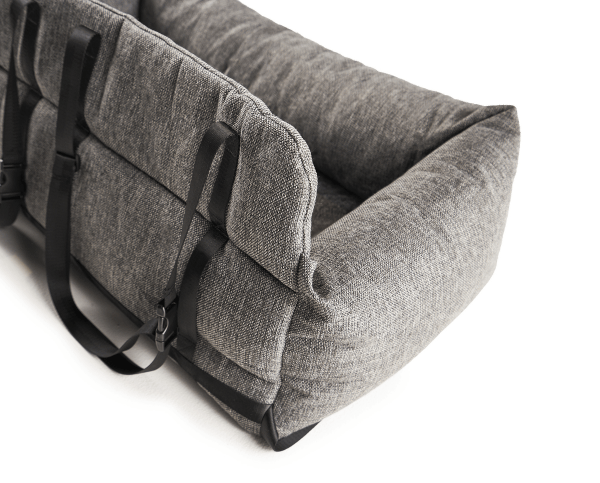 Gray dog car bed with side carry handles and attached securing straps.