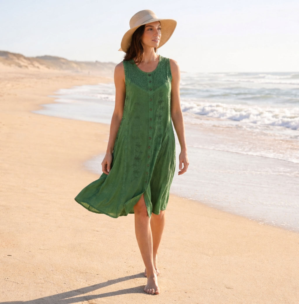 Green sleeveless midi dress with embroidered pattern; model walking outdoors on beach.