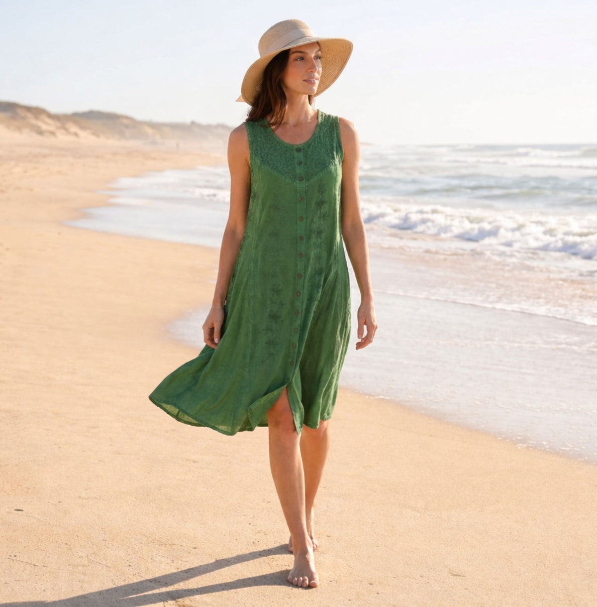 Green sleeveless midi dress with embroidered pattern; model walking outdoors on beach.