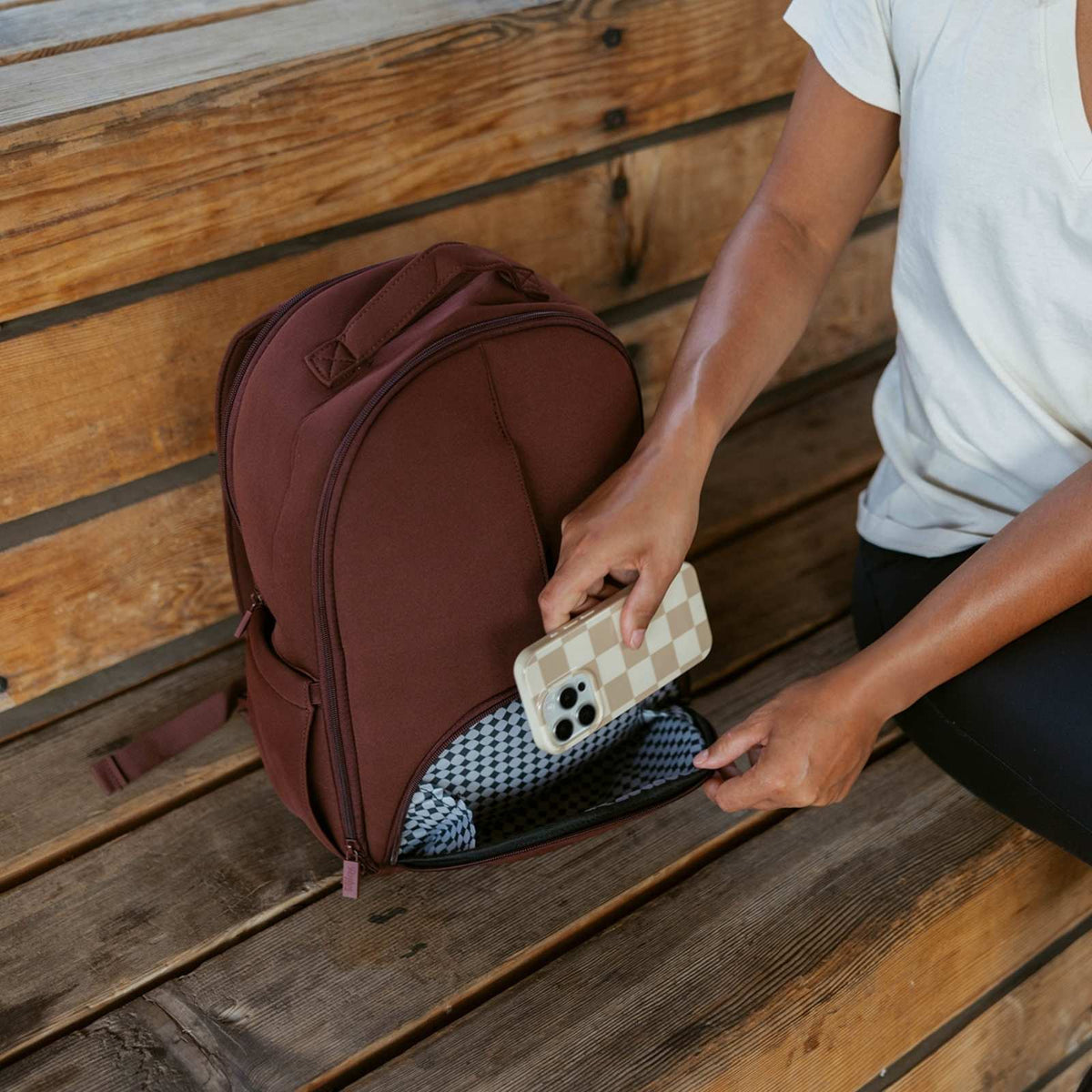 Raisin brown neoprene diaper backpack, front zip pocket holding a smartphone