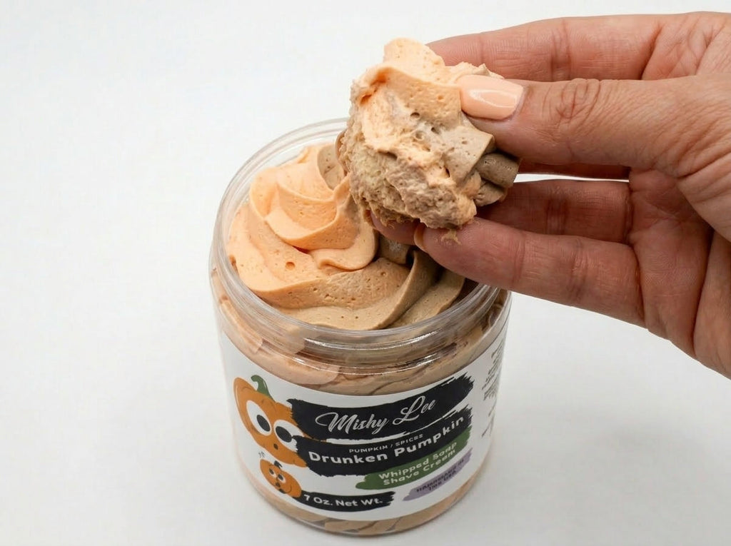Hand holding a scoop of orange whipped soap from a clear jar