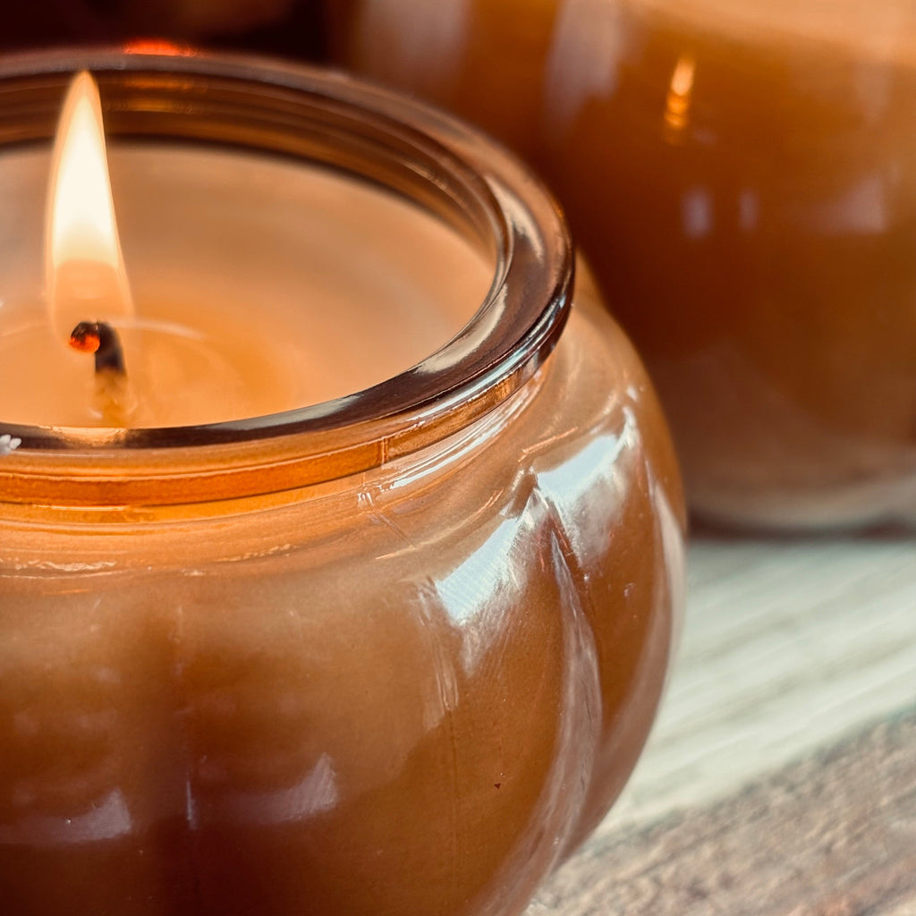 Amber soy candle jar with lit wicks and glossy glass rim, close-up view