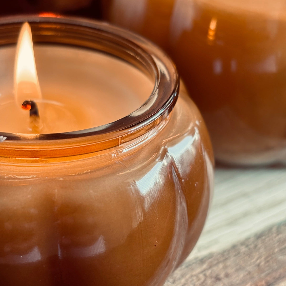 Amber soy candle jar with lit wicks and glossy glass rim, close-up view