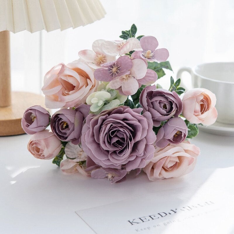 Lavender and pale pink silk rose bouquet with green leaves in a clear vase