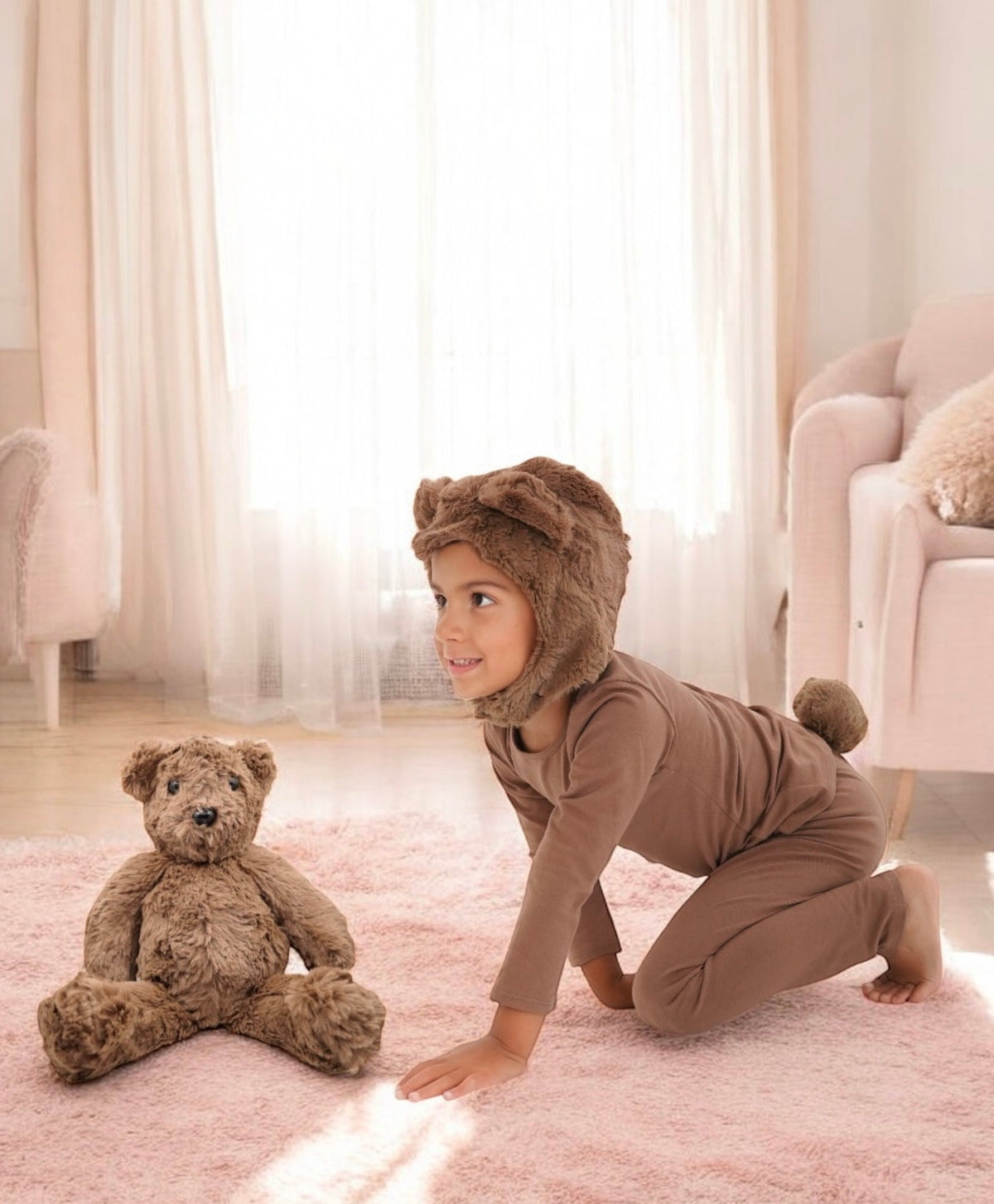 Brown plush teddy bear on the floor with a child kneeling beside it.