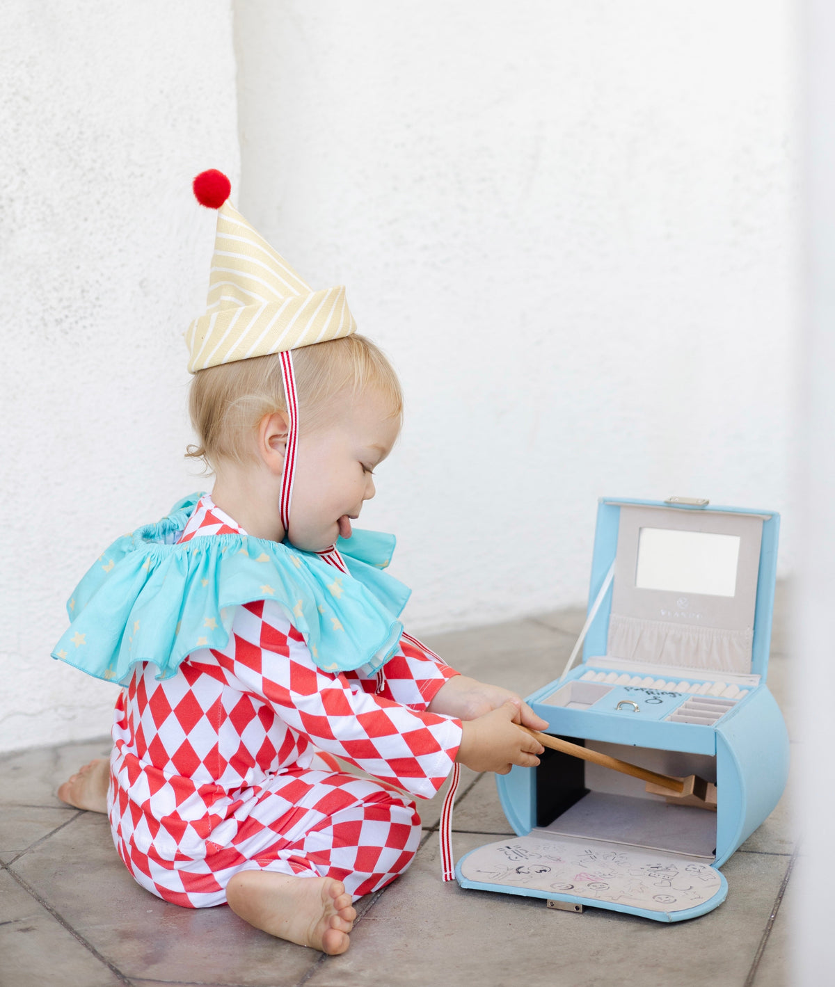 Kids clown costume seated: red-and-white diamond jumpsuit, light blue ruffled collar, striped hat