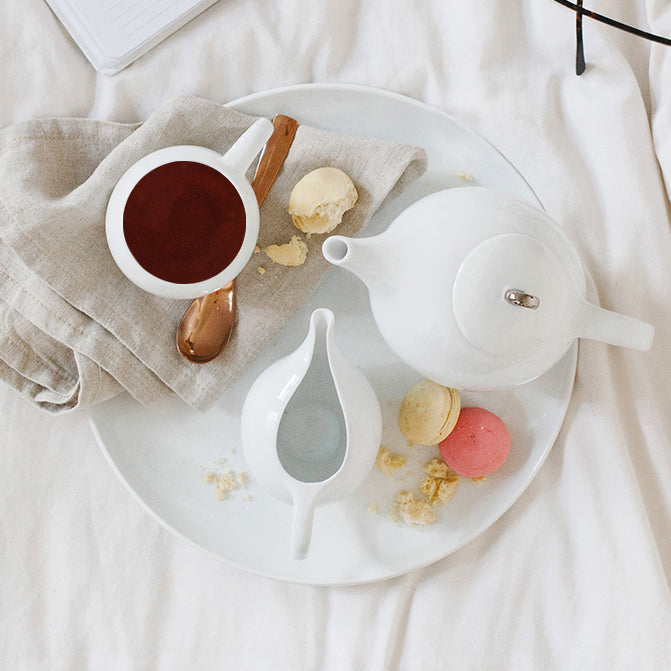 White ceramic teapot with infuser and lid on a serving plate