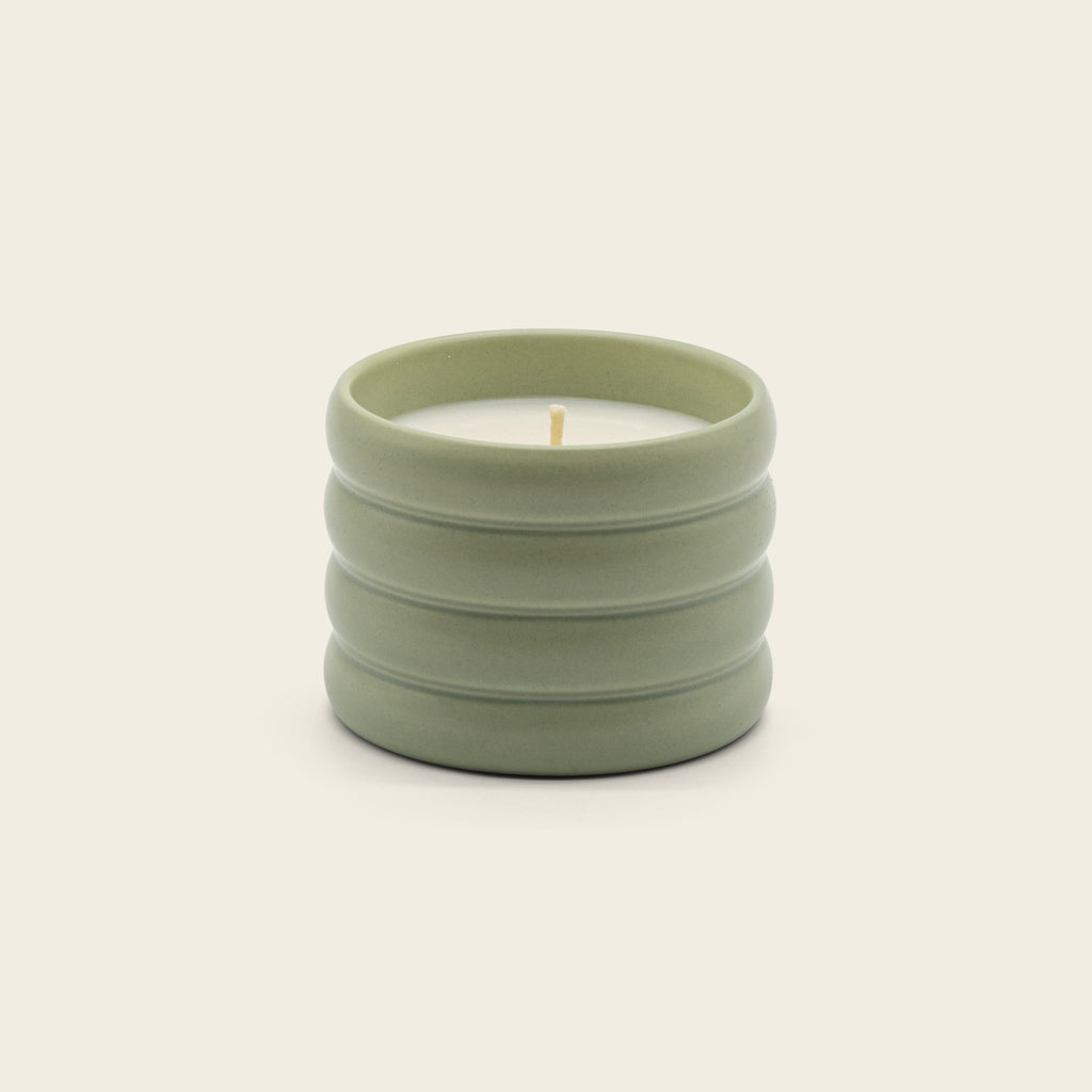 Sage green ceramic soy candle with lit wick in ribbed stoneware vessel.