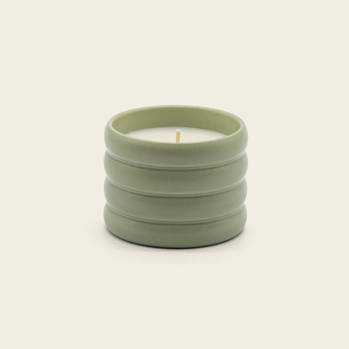 Sage green ceramic soy candle with lit wick in ribbed stoneware vessel.