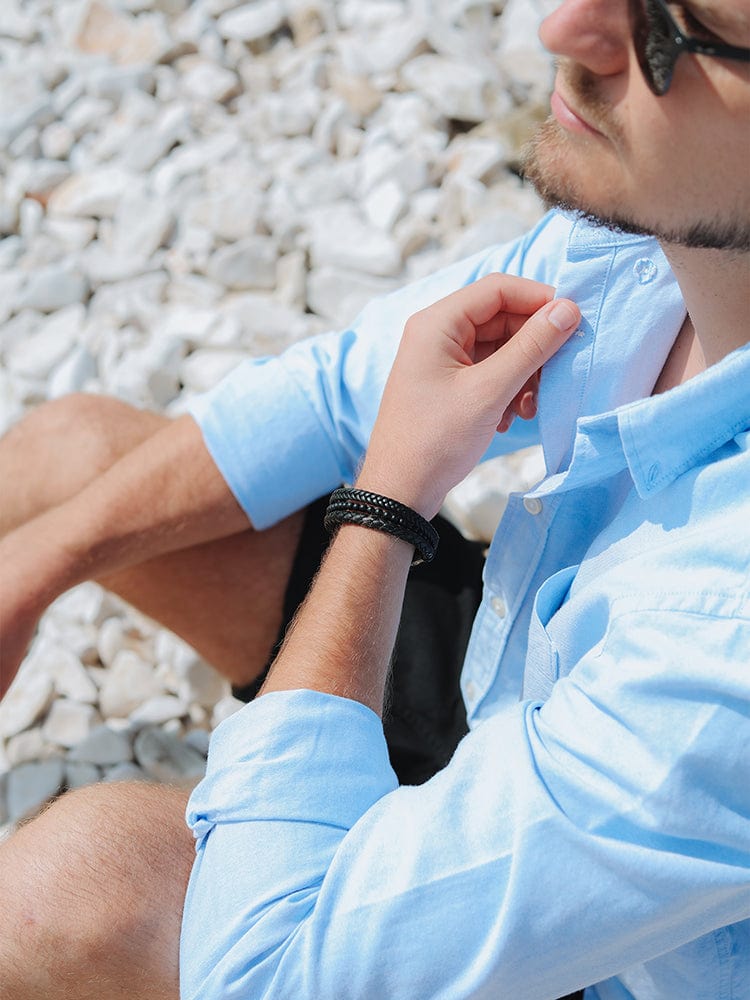 Black braided leather bracelet with bead rows on wrist while adjusting shirt.