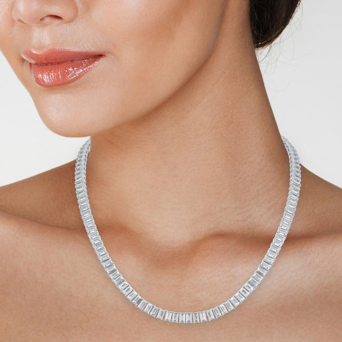 Emerald-cut tennis necklace on neck, clear rectangular stones in silvery setting