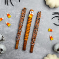 Three Halloween pretzel rods, orange and black sprinkle coating on ridged pretzel