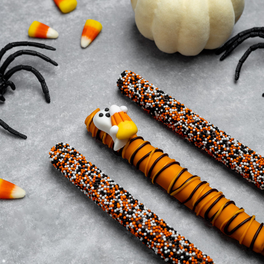 Three Halloween pretzel rods with candy corn heads and orange-black sprinkle coating