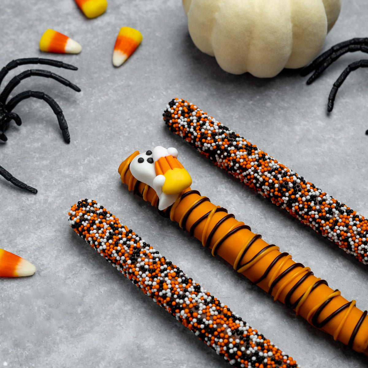 Three Halloween pretzel rods with candy corn heads and orange-black sprinkle coating