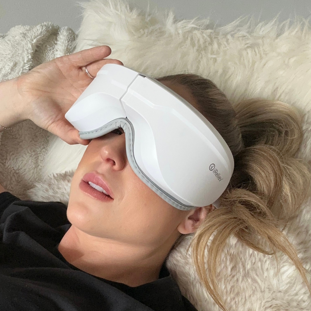 Heated eye massager with gray strap resting on a person’s closed eyes