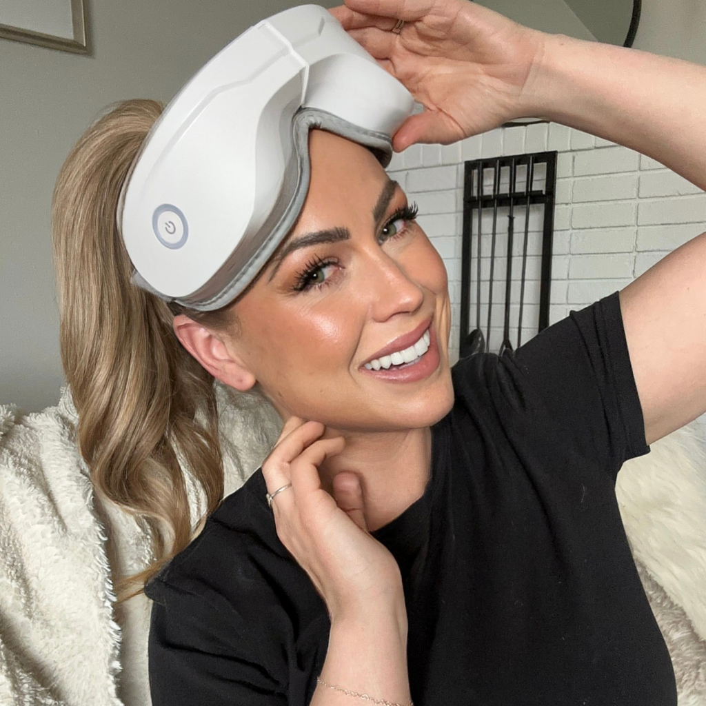 Heated eye massager being positioned on closed eyes with gray strap