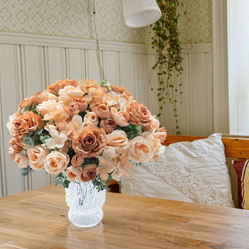 Peach and orange silk rose bouquet with green foliage in a clear glass vase