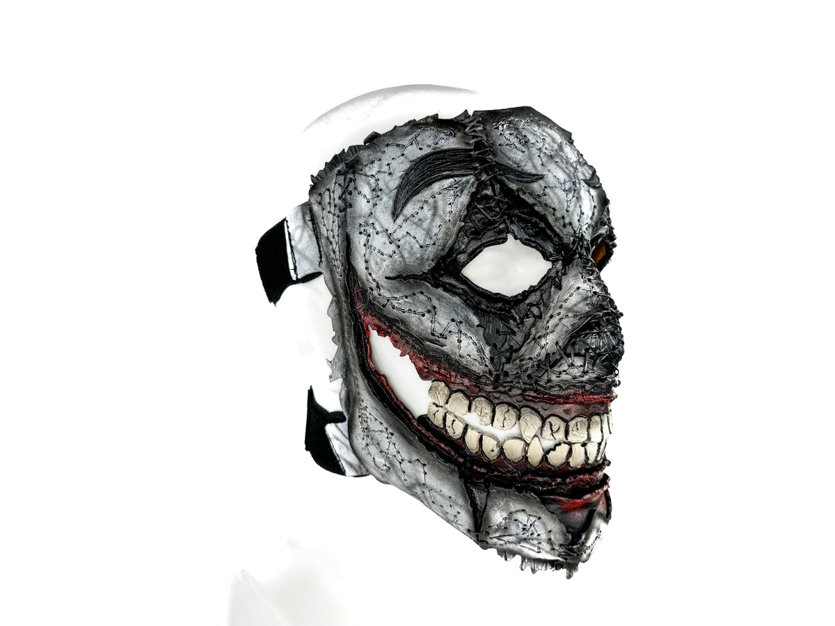 Gray leather full-face mask with eye and mouth openings, red trim line, detailed teeth
