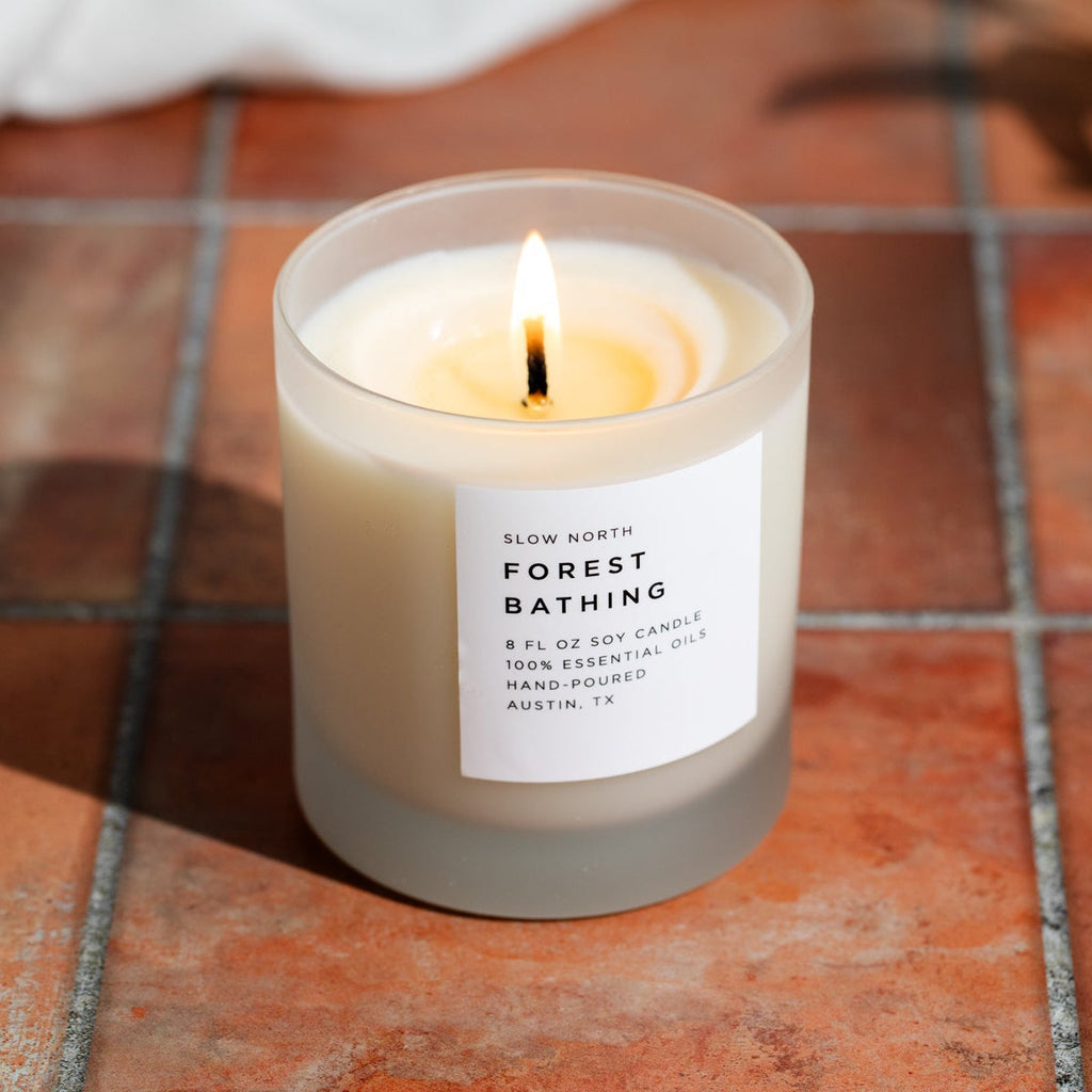 Soy candle in frosted jar with lit wick, white label on gray base