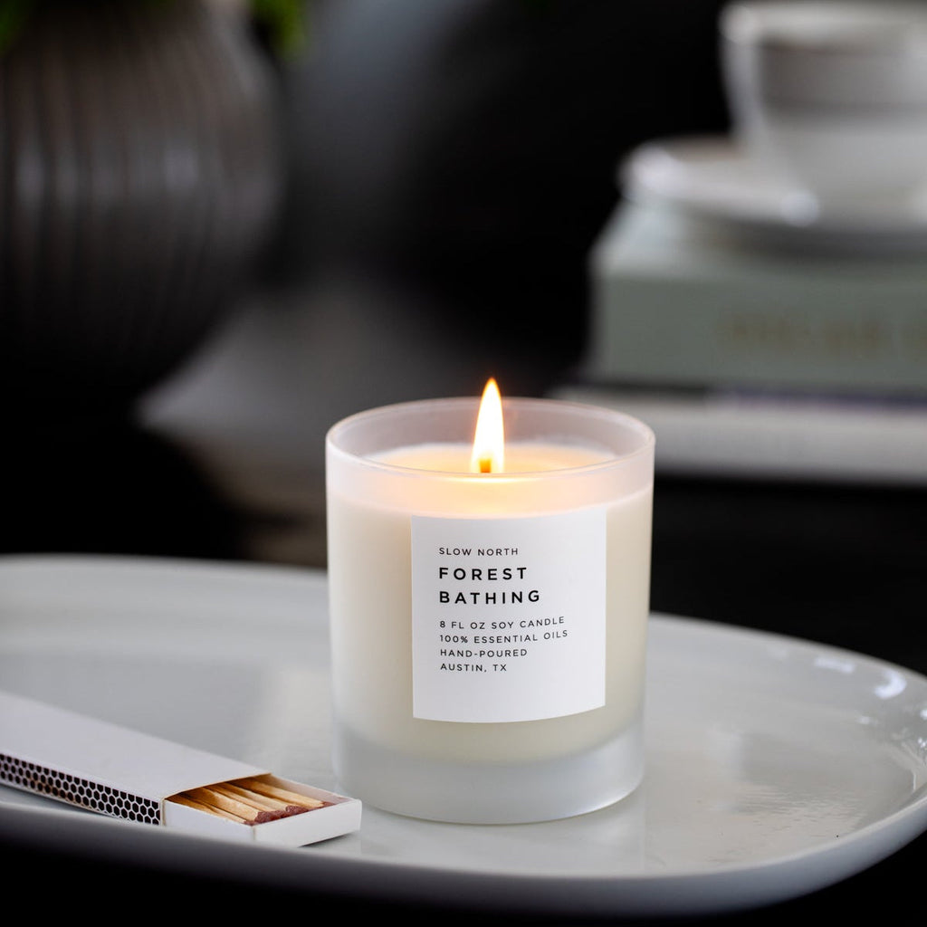 Soy candle with lit wick and white label on frosted jar atop a serving tray