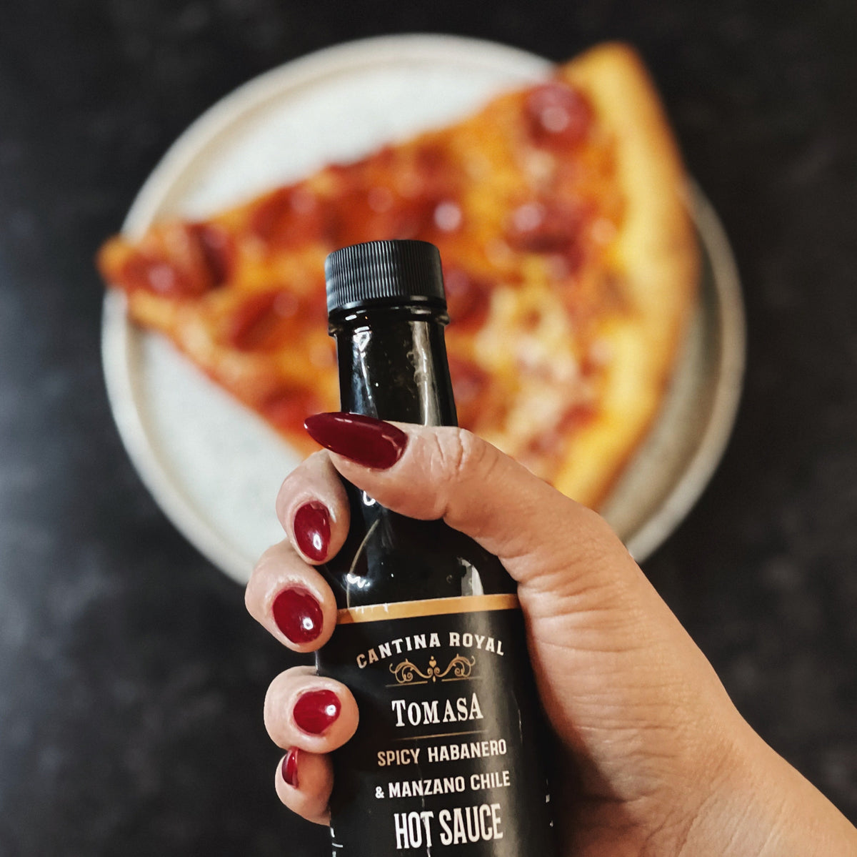 Hot sauce bottle held in a hand, black cap and label with spicy habanero.
