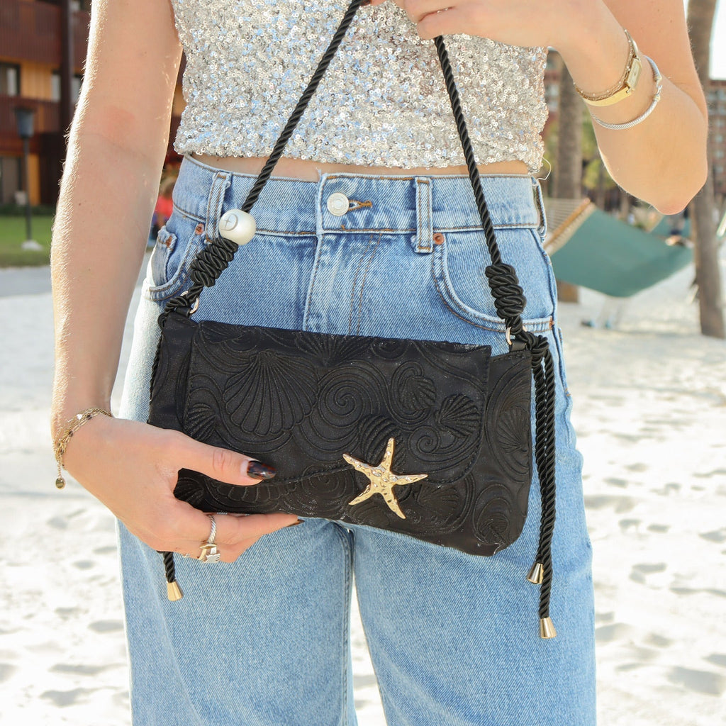 Black shoulder bag worn crossbody with starfish front clasp and braided tassel cords