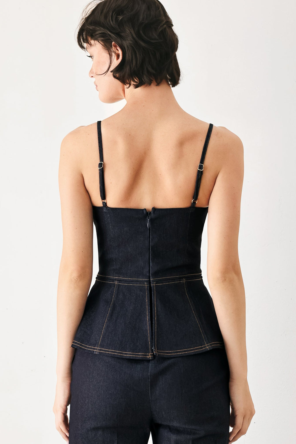 Back view dark denim jumpsuit with thin straps, centered seam, peplum waist