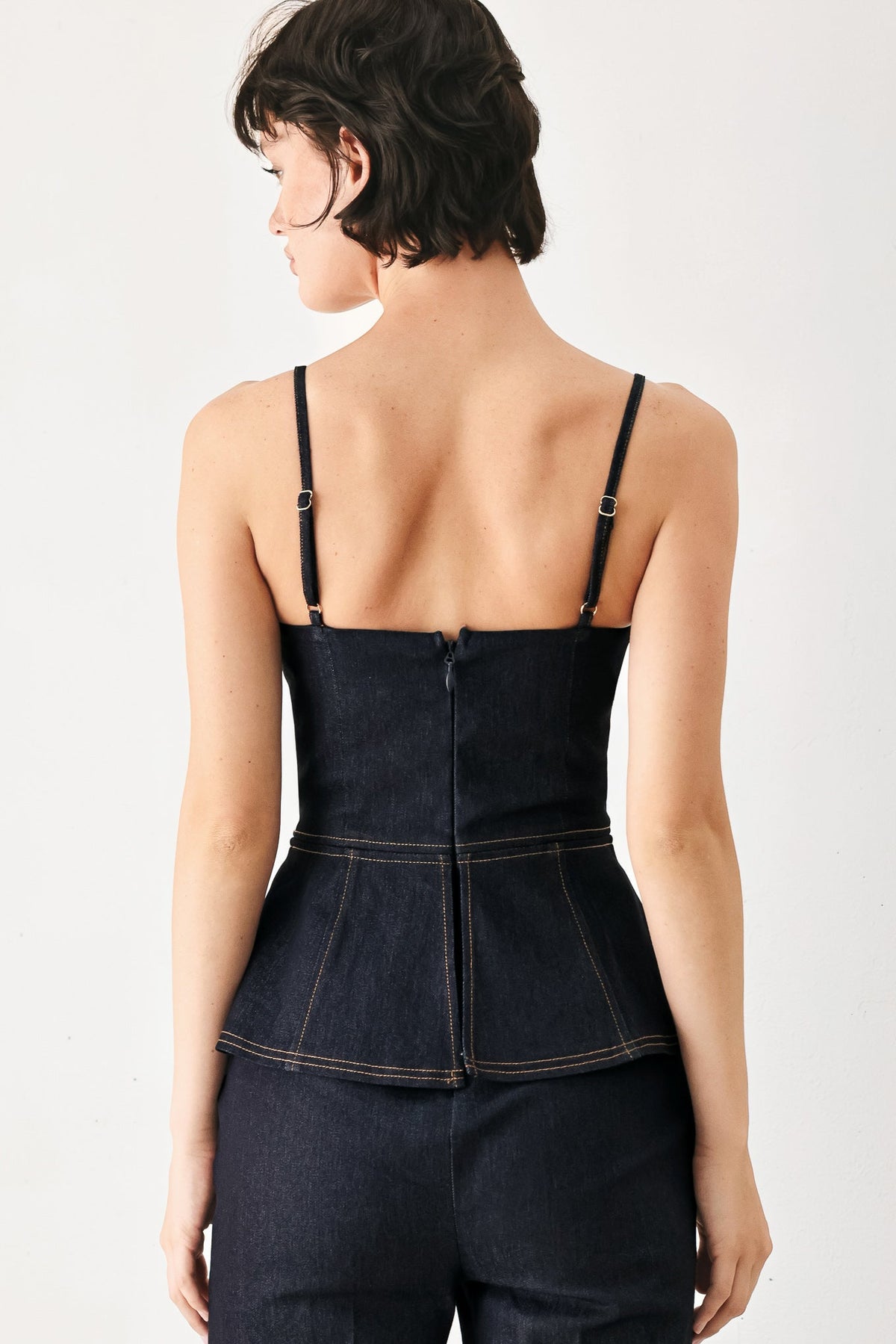 Back view dark denim jumpsuit with thin straps, centered seam, peplum waist
