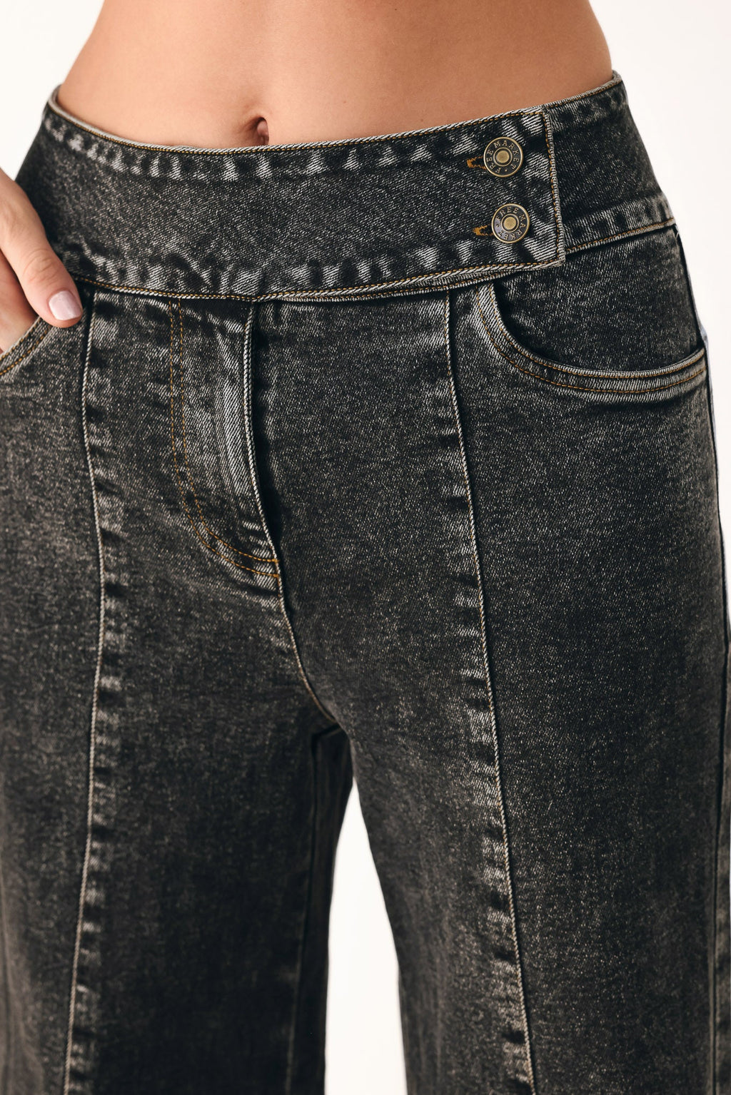 Close-up of black wash denim waistband with button details and stitched pockets