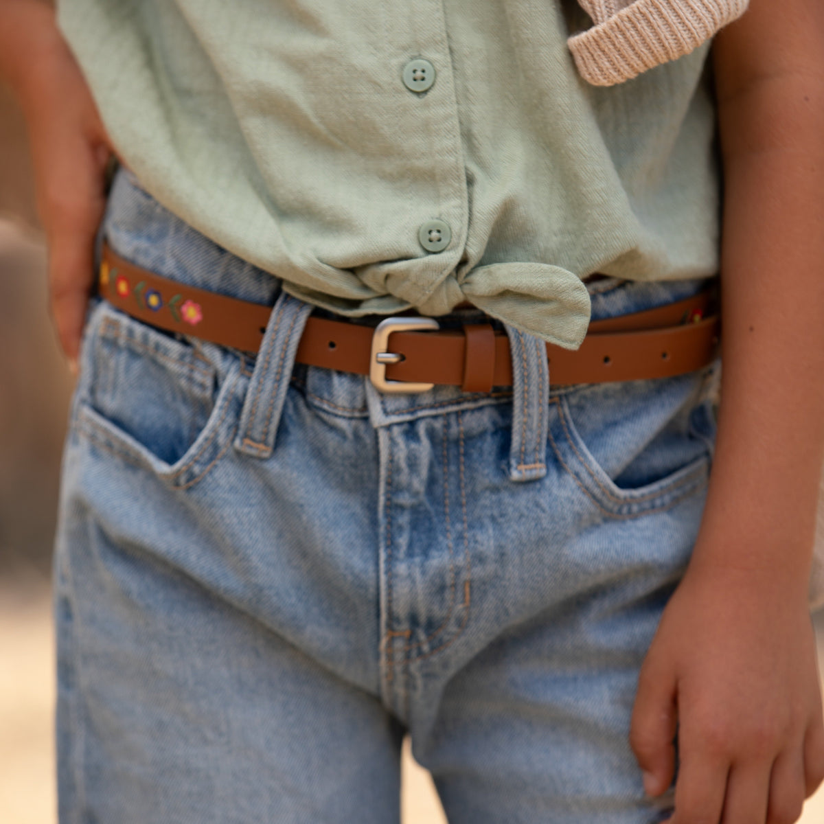 Kids leather belt on denim: brown floral-embroidered strap with silver buckle