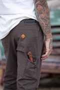 Dark brown taper-fit pants close-up: cargo pocket with logo patch and stitched details.