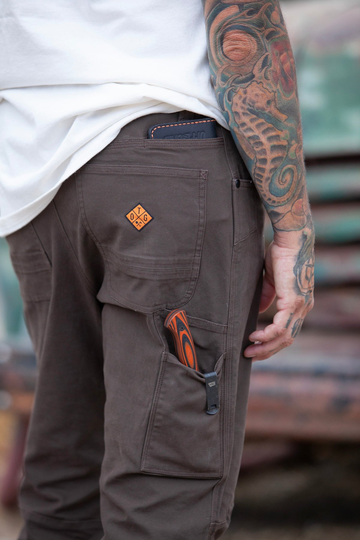 Dark brown taper-fit pants close-up: cargo pocket with logo patch and stitched details.