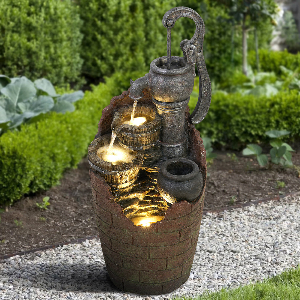Barrel outdoor fountain featuring hand pump spout, stacked basins, and glowing light accents