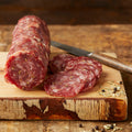 Fennel & white wine salami, sliced, with herbs and spices on a wooden board