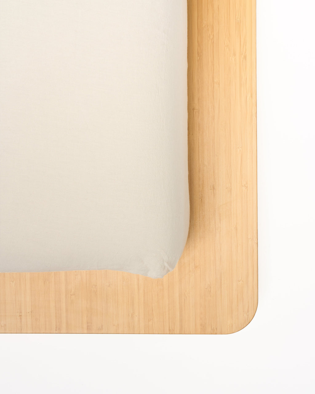 Cream fitted sheet corner with elastic edge neatly draped over a wooden base