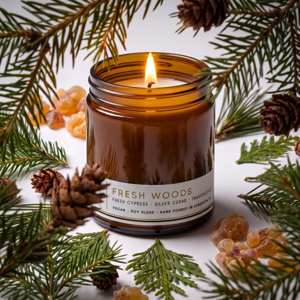 Amber glass candle jar with lit wick and Fresh Woods label, glossy brown wax