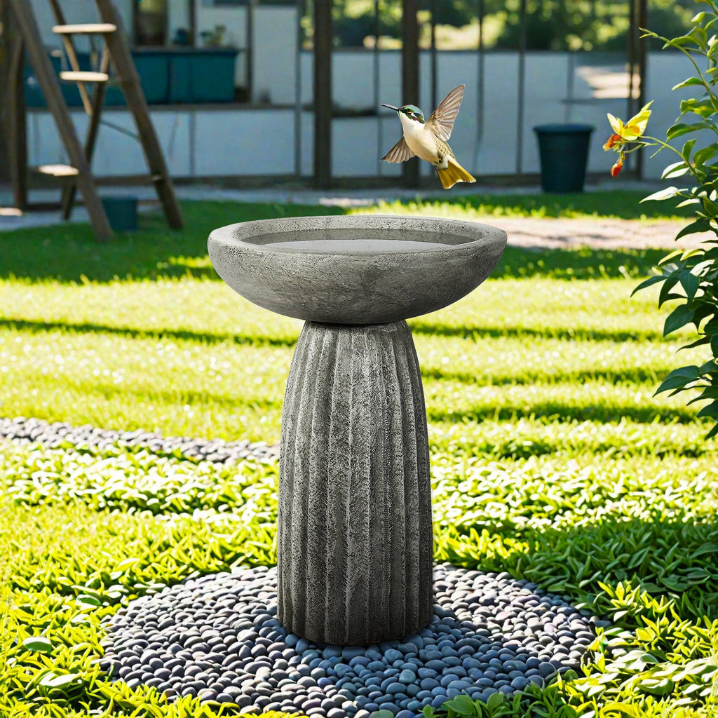 Concrete bird bath with round bowl and fluted pedestal in garden setting