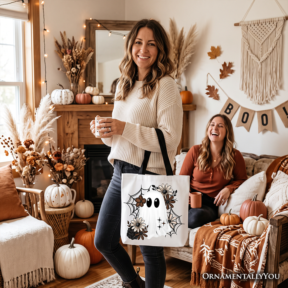 Beige tote bag with black handle and floral ghost graphic, carried by woman