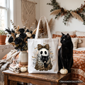 White tote bag with black handle tops, ghost cat graphic in leopard bow and web art