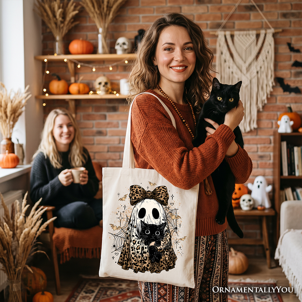 White tote bag with black cat and ghost illustration, leopard bow, and spiderweb motifs